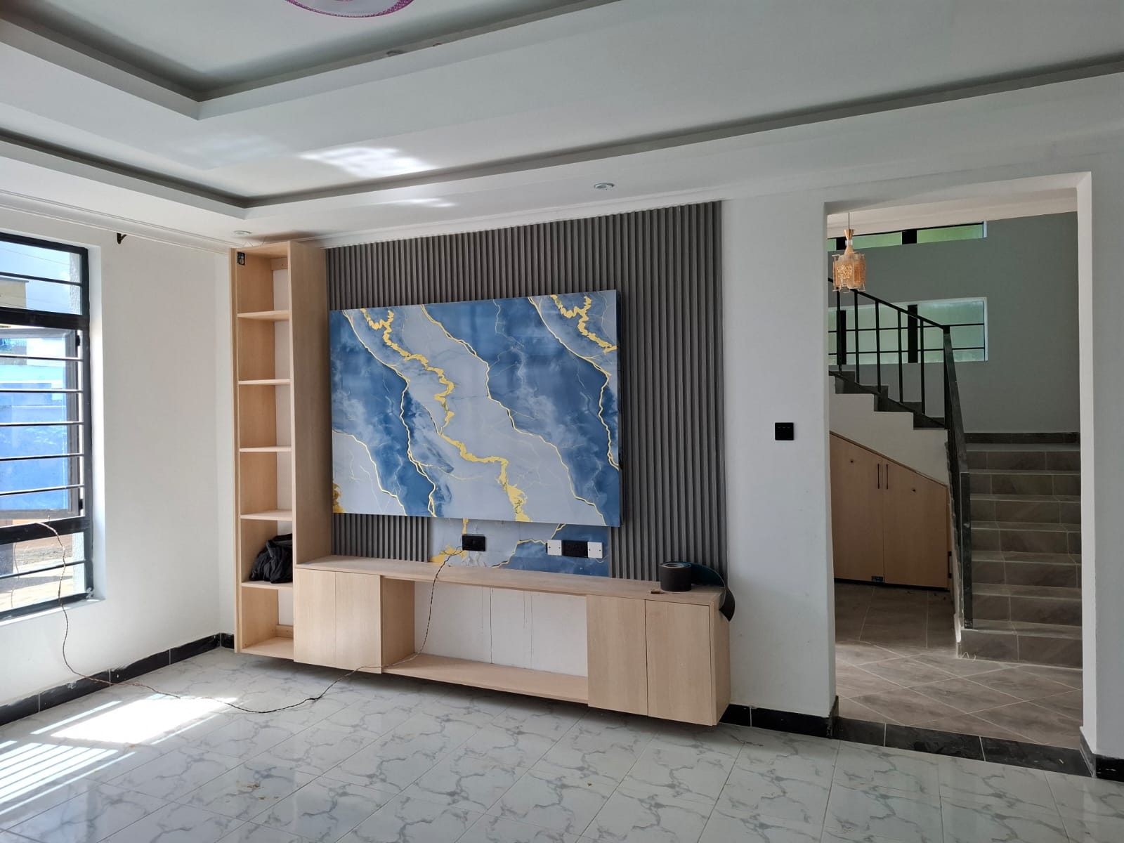 Modern living room TV feature wall with vertical fluted charcoal panels, gold metal trim, and white marble quartz slab